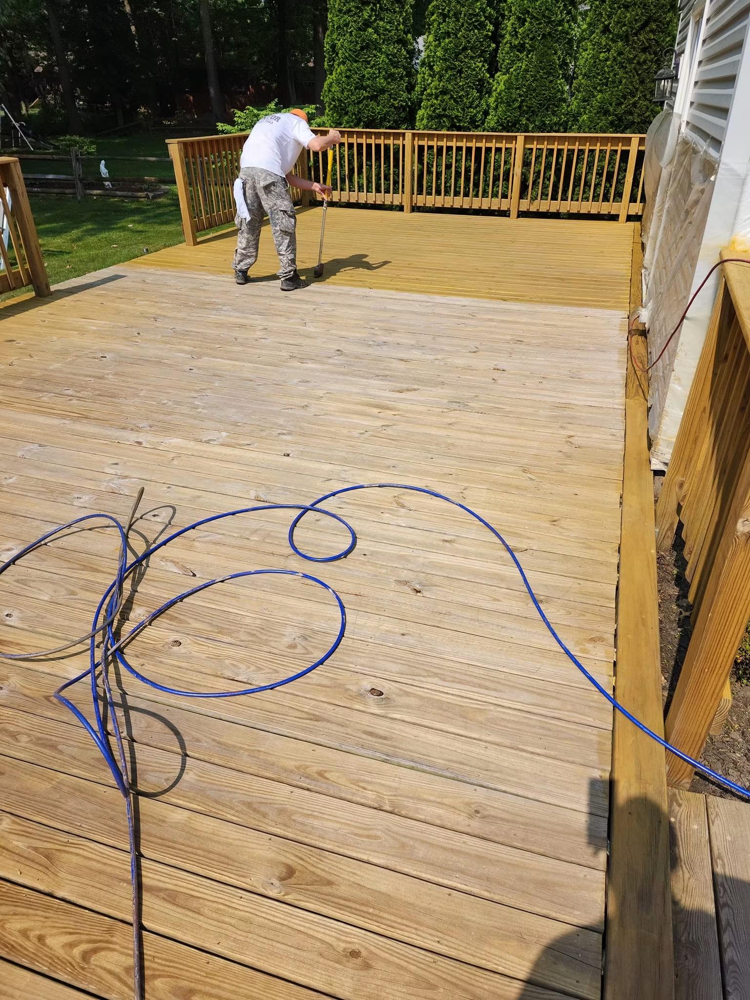 Brian applying stain to a deck, wearing a Mentor Painting & Staining shirt